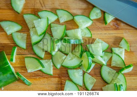 Pieces of cucumber for salad on a wooden cutting board and cook knife