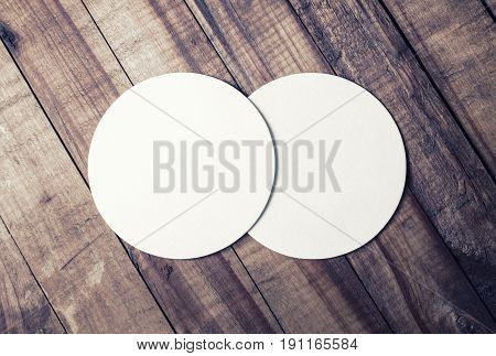 Photo of two blank white beer coasters and coffee beans on wood table background. Blank template for your design. Top view.