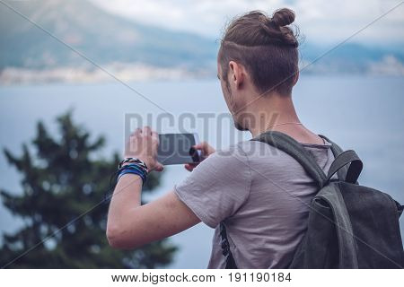 Man Traveler With Backpack Makes A Photo On Your Smartphone Outdoors With Mountains In The Backgroun