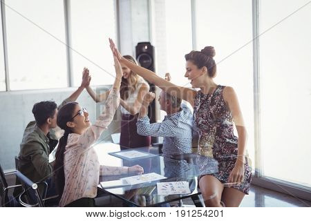 Happy business colleages giving high five at creative office desk