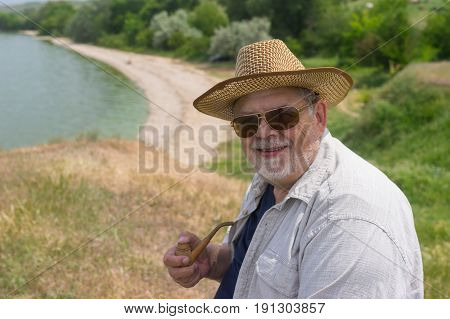 Outdoor portrait of happy senior man in dark sunglasses and straw hat