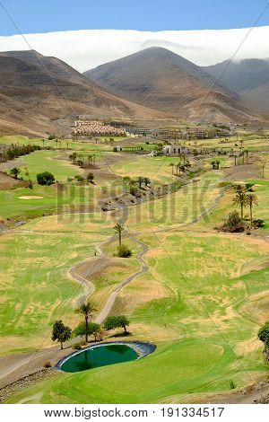 View on the green field for golf between the mountains a beautiful whte cloud and blue sky on the Canary Island Fuerteventura Spain.