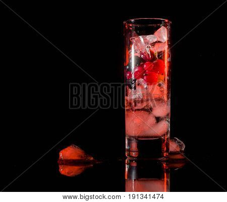 Glass of ice with berry gooseberries red black currants and water. Refreshing cocktail. Summer drink. Dark background.