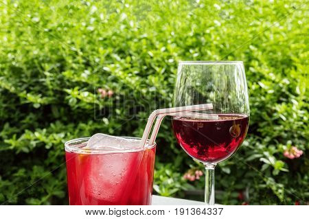 A glass of tinto de verano, a Spanish summer cocktail, and a glass of red wine, on a terrace in a garden, with a place for text. Selective focus