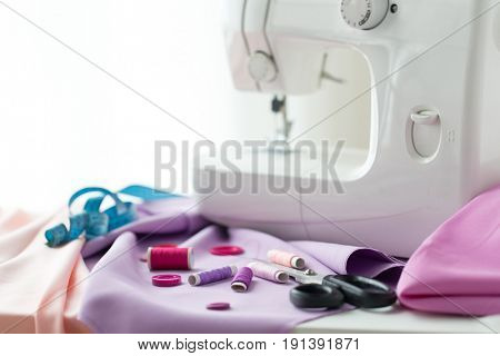 needlework, technology and tailoring concept - sewing machine with scissors, buttons, tape measure and fabric