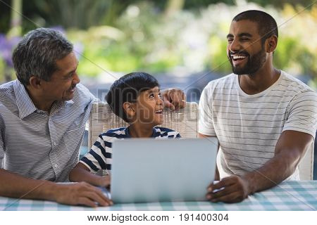 Happy multi-generation family sitting by laptop on table at porch