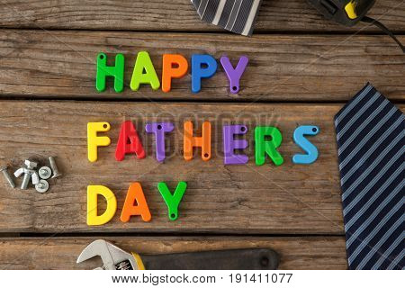 Close-up of happy fathers day blocks, tie and handtools on wooden plank