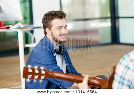 Students sitting on the floor with one playng guitar