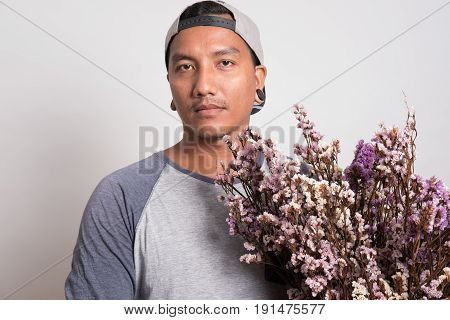 Asian Young Man Wearing Casual T-shirt And Cap Holding A Bouquet Of Purple Flower Standing Against A