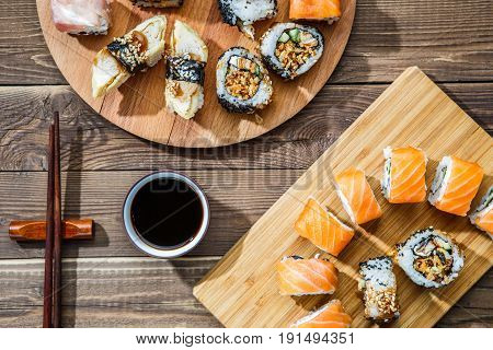 Two sets of rolls on wooden plates on table with soy sauce and chopsticks