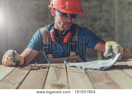 House Construction Contractor with Installation Documentation on the Wooden Table. Construction Worker Reviewing Docs.