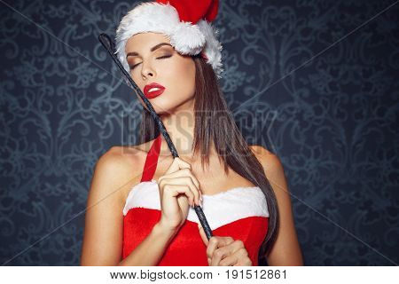 Sexy santa girl posing with whip at vintage wall sensuality and desire