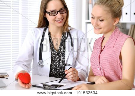 Doctor showing heart model to his patient and pointing into confidental medical history