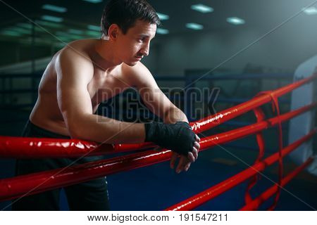 Boxer in black bandages poses on ring ropes