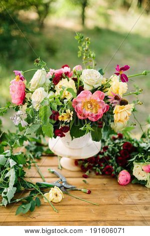 arts and crafts, wedding, decor, celebration, summer, nature concept - bunch of ornamental flowers like peonies, roses, avalanches and diathuses, decorated with verdure, placed in vase on wooden table