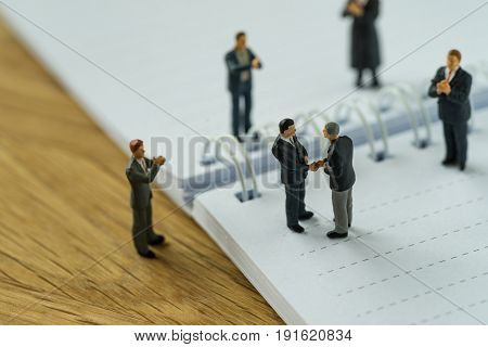 Miniature people with small figure businessmen handshaking and others clapping on notebook and pencil as business agreement concept.