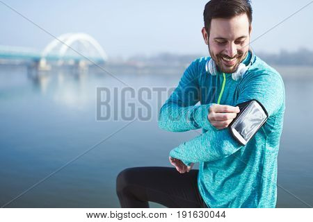 Handsome sportsman using phone to listen to music while running and jogging