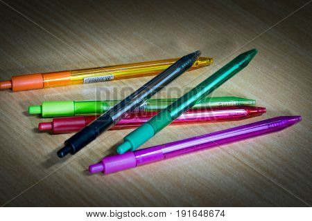 Many Bright colored Ballpoint pens on wooden desk.