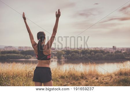 Sporty woman enjoys exercising and looking at city view with her arms outstretched.