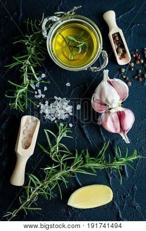 Herbs and spices selection - rosemary garlic lemon salt peppercorns and olive oil on dark stone table. Cooking ingredients concept. Food flat lay. Top view.