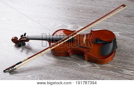 Violin with bow isolated on wooden background. Classical stringed musical instrument fiddle with fiddlestick.