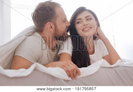 Duvet dalliances. Young man and woman smiling while lying in bed and making a declaration of love together.