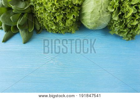 Green vegetables lettuce and herbs at border of image with copy space for text. Top view. Cabbage spinach dill and lettuce. Green vegetables on a blue background.