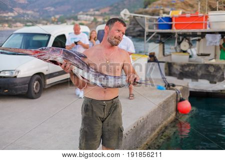 Bali Island Crete Greece - June 30 2016: Man is a fisherman carries a big fish (sawfish) after successful fish catch from the fishing boat.