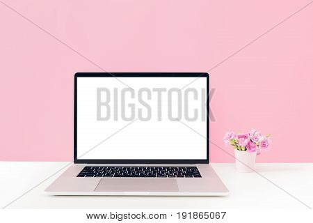 Laptop with white blank screen and flowers in a vase on a table on a pink background. mock up
