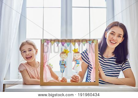 Happy loving family. Mother and her daughter in kids room. Funny mom and lovely child having fun and playing performance in the puppet theater indoors. Prince and princess.