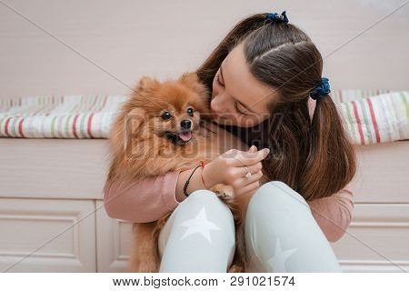 Teenage Girl With A Dog Breed Spitz Rejoices With A Pet At Home On The Floor. Care And Training Of A