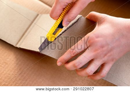 Paper Knife In Person Hands Cutting Cardboard Piece. Cardboard Background. Close-up.