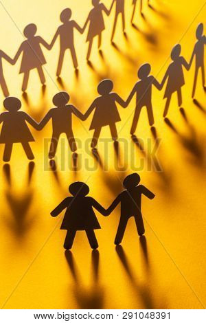 Black paper figure of a couple in front of a crowd of paper people holding hands on yellow surface. Social movement, protest, leadership concept.