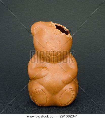 Chocolate Bear With Bitten Off Ear On Dark Green Background.