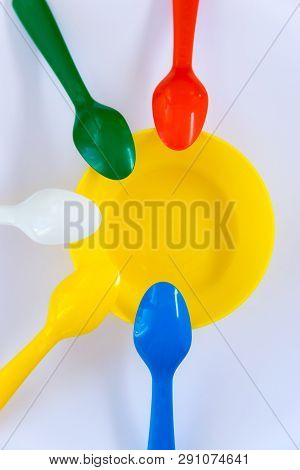 Plastic Multicolor Spoons Located Around Yellow Plate On The White Background. Flat Lay. Top View. M