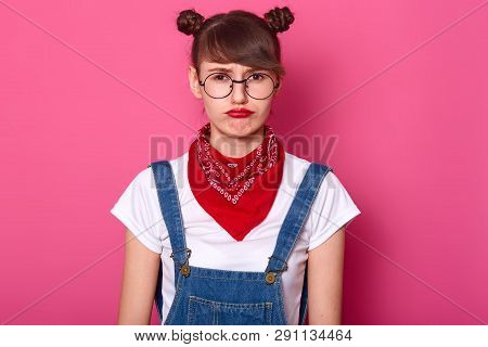 Upset Young Female Model Looks Offened, Being In Bad Mood, Stands Alone And Looks Directly At Camera