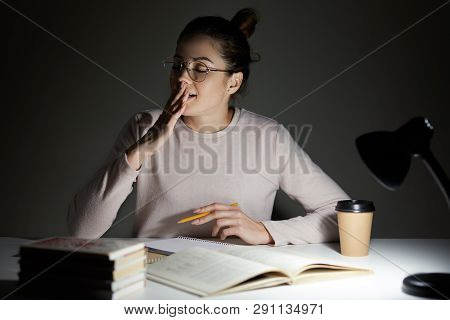 Image Of Attractive Seepy Student Yawns With Closed Eyes, Sits At Desktop While Preparing For Classe