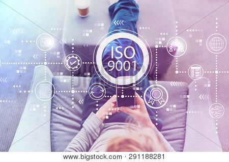 Iso 9001 With Man Using A Smartphone In A Modern Gray Chair