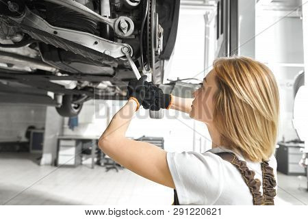 Blonde Woman Working As Mechanic In Autoservice, Repairing Car Undercarriage, Using Wrench. Concentr