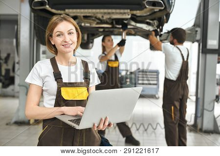 Beautiful Young Woman, Worker Of Autoservice Posing, Holding Laptop In Hands. Pretty Girl Looking At