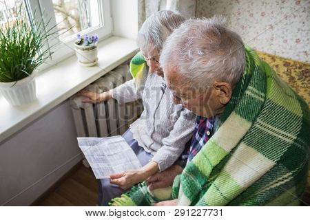 The Senior Woman Holding Gas Bill In Front Of Heating Radiator. Payment For Heating In Winter.