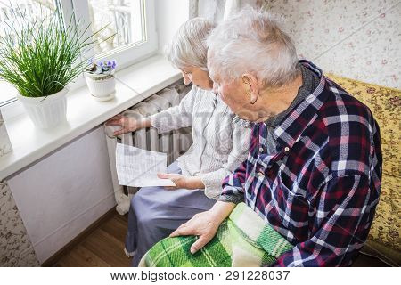 The Senior Woman Holding Gas Bill In Front Of Heating Radiator. Payment For Heating In Winter.