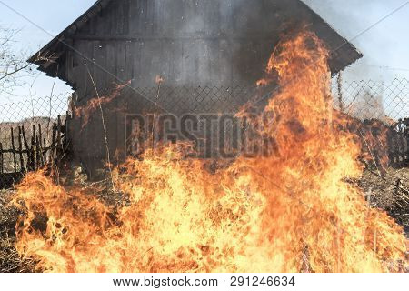 Burning Grass. Fire Outdoors. Behind The Wooden House