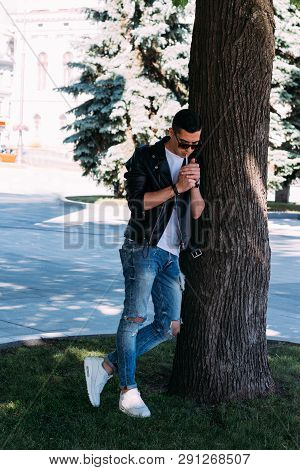 A Young Guy Smokes Around A Tree In The City.bad Habit.smoking In A Public Place