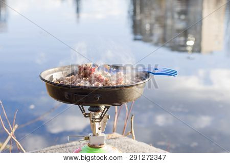 Warming up food in a pan. Tourist gas stove and frying pan. Heated buckwheat porridge.