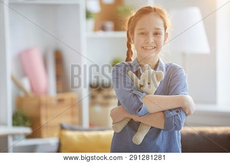 Waist Up Portrait Of Happy Red Haired Girl Hugging Plush Toy And Looking At Camera Lit By Warm Sunli