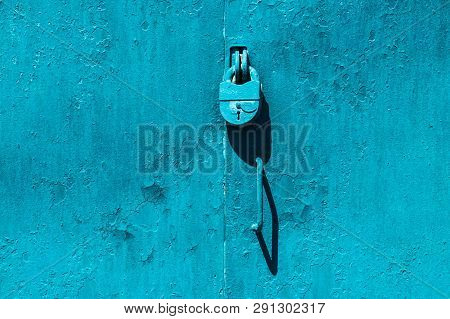 Closed Imperfect Blue Garage Gate With Padlock Close-up. Texture Of Locked Iron Door With Cyan Peeli