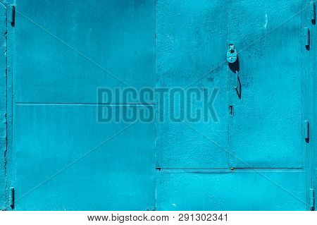 Closed Imperfect Blue Garage Gate With Padlock Close-up. Texture Of Locked Iron Door With Cyan Peeli