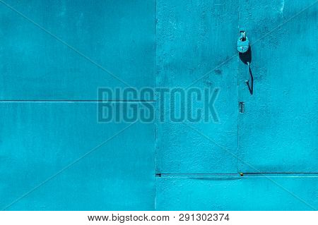 Closed Imperfect Blue Garage Gate With Padlock Close-up. Texture Of Locked Iron Door With Cyan Peeli