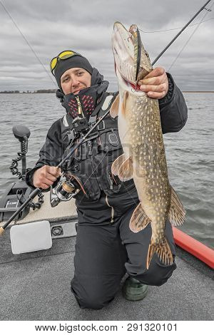 Happy Fisherman With Big Pike Fish Trophy At The Boat With Fishing Tackles